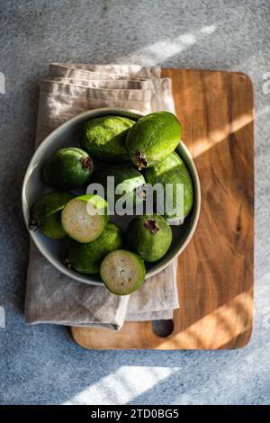 A bowl of ripe feijoa fruits, some cut in half, beautifully presented on a wooden kitchen board with a linen napkin under natural lighting. Stock Photo