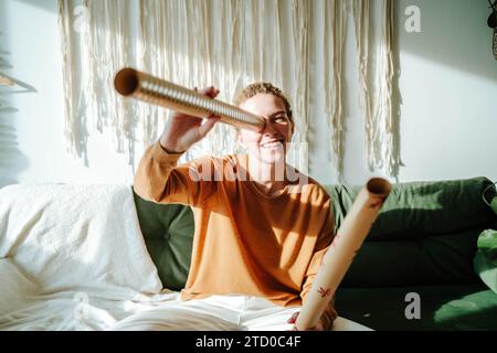 Smiling young female sitting on comfortable sofa and holding wrap for Christmas presents while having fun at home Stock Photo