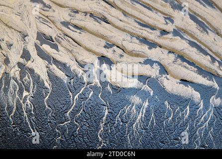 A captivating aerial view of natural patterns created by sand and water interaction on a beach, showcasing textural contrasts. Stock Photo