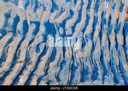 Abstract natural art of wavy sand patterns highlighted with deep blue shadows, showcasing textures and forms created by light and shade. Stock Photo