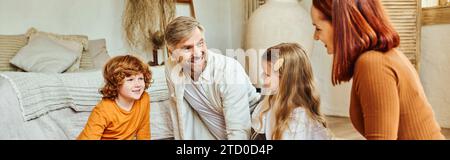 joyful parents with daughter and son looking at each other in living room at home, horizontal banner Stock Photo