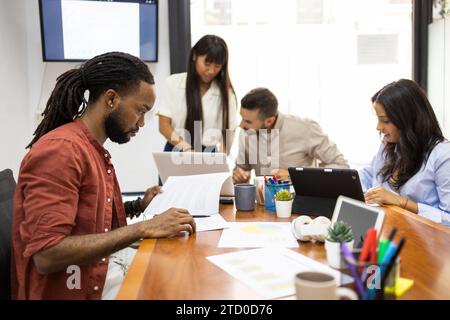 Serious business people examining documents and using tablet while colleagues discussing over laptop in background during meeting in office Stock Photo