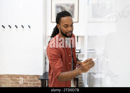 Smiling African American young businessman writing on whiteboard with felt tip pen during meeting in coworking office Stock Photo