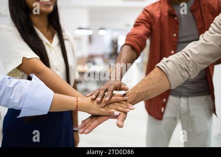 Crop hands of anonymous of multiracial male and female colleagues stacking hands together while standing in creative office Stock Photo