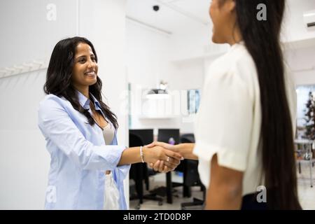 Smiling young businesswoman handshaking with anonymous colleague while standing in corridor at creative office Stock Photo