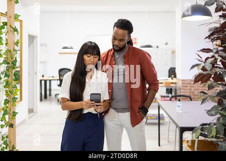 Multiracial serious focused coworkers dressed in casuals discussing over mobile phone while standing in creative office Stock Photo