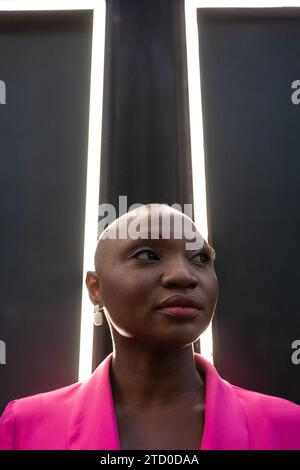 Confident African American female with shaved head in pink outfit and earrings looking away while standing in front of frames with light in between wi Stock Photo