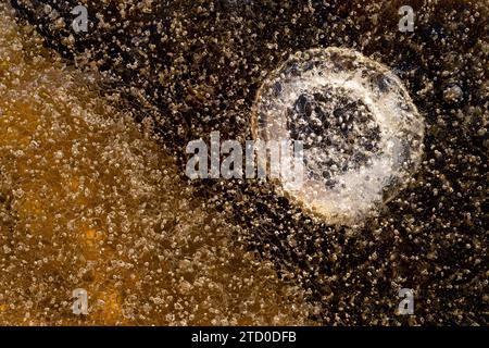 Top view textured background of frozen water surface with small bubbles and round shaped crack in winter Stock Photo