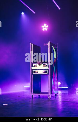 Magician showing magic trick with disappearing body in box on dark stage illuminated by purple neon spotlights Stock Photo