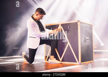 Full body of male illusionist in white jacket locking box on stage with smoke while doing magical trick in theater Stock Photo