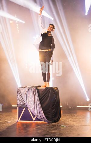 Full body of illusionist standing on top of box with fabric and raising hand while performing magic trick on stage in theater Stock Photo