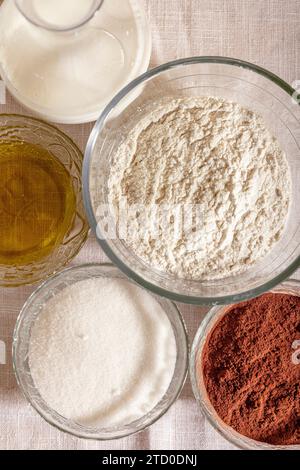 Overhead view of glass bowls filled with flour, sugar, cocoa, oil, and milk, ready for baking placed on table Stock Photo