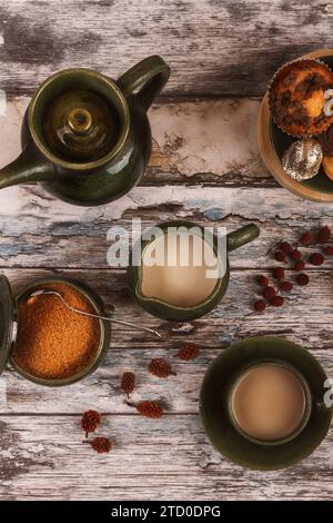 A top-down view of a cozy tea arrangement featuring two cups of tea, a green teapot, spices, and dried fruits on a rustic wooden table. Stock Photo