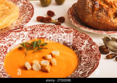 A heartwarming serving of salmorejo garnished with croutons and parsley, accompanied by a rustic loaf of bread, all laid out on decorative plates. Stock Photo