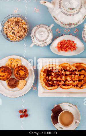 A top-down view of an elegant tea time spread featuring snacks, a tea pot, and a cup filled with tea on a blue background. Stock Photo