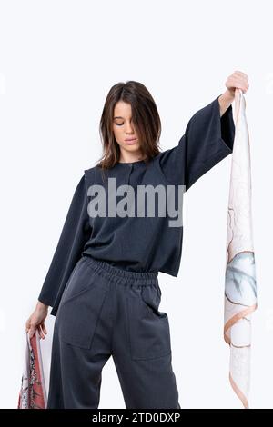 Young woman in casual clothes with dark hair showing leaf pattern fabric while standing eyes closed against white background Stock Photo
