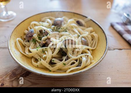 Freshly cooked delicious fettuccine pasta with clams served in plate with cutlery and napkin on wooden table at restaurant Stock Photo