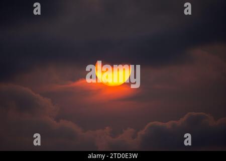 A striking image of a partial solar eclipse captured as the sun peeks through moody, dark clouds, creating a haunting backdrop. Stock Photo