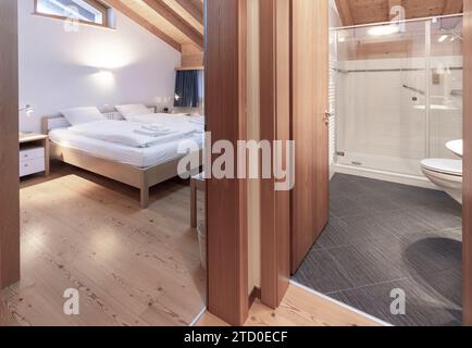A neatly-kept bedroom and bathroom featuring a large bed with white bedding and an en suite bathroom, showcasing a clean, contemporary design with woo Stock Photo