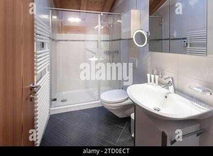 A sleek, modern bathroom featuring a glass shower, white tiles, and wooden detailing. Stock Photo