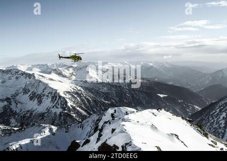 Picturesque view of helicopter flying above majestic rocky snowcapped mountains located against sky during sunny day in winter Stock Photo