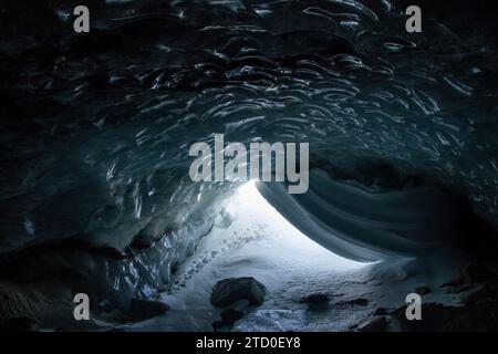 Interior of breathtaking frozen cave with snow covered rocky field and uneven holes in rough ice surface during winter in Canada Stock Photo