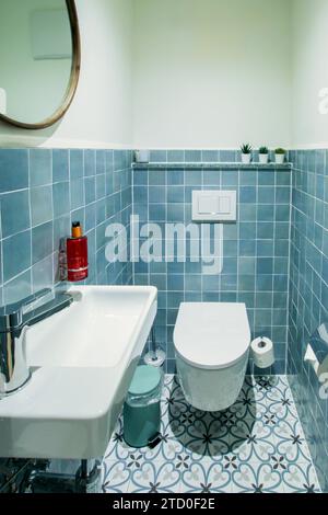 Interior view of a modern bathroom featuring white fixtures, blue wall tiles, decorative floor tiles, and minimalist decor. Stock Photo