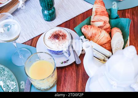 A sophisticated brunch table featuring a cappuccino, croissants, bread, and orange juice with a soothing background. Stock Photo