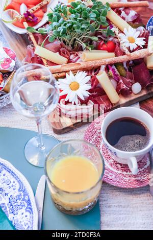 A stylish charcuterie board filled with assorted meats, cheese, and fresh garnishes, accompanied by wine, fresh juice, and coffee. Stock Photo