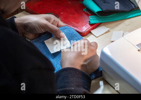 Close-up of hands sewing a blue fabric with needle and thread at a workbench with sewing accessories. Stock Photo