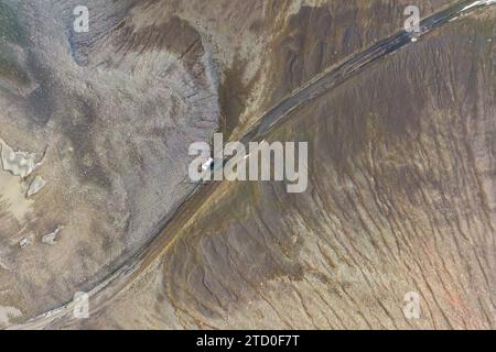 An aerial shot showcases a car traveling on road meandering through the brown and textured landscape of the Icelandic highlands, near Thorsmork valley Stock Photo