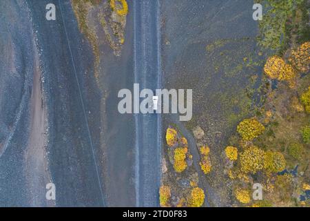 An aerial shot capturing a lone car with opened doors and an anonymous person standing near it on road surrounding by rugged landscapes of the Thorsmo Stock Photo