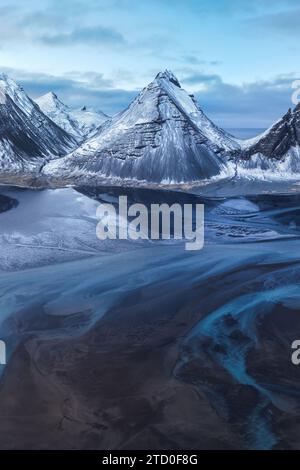 Snow blankets the rugged peaks of an Icelandic mountain range with a striking glacial stream winding through the valley. Stock Photo