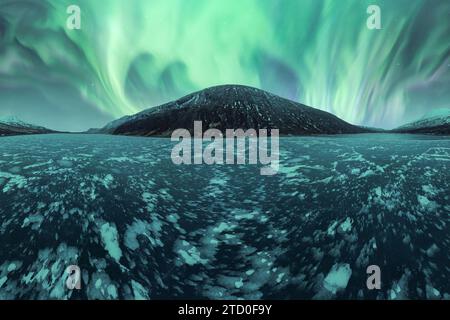 Ethereal aurora borealis unfolding over a snow-covered volcano in the tranquil Icelandic landscape. Stock Photo