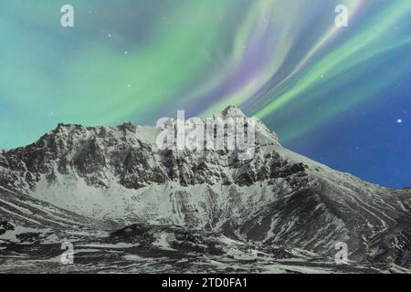 A stunning view of the Northern Lights dancing above a snow-covered mountain in the Icelandic wilderness, creating a magical winter scene. Stock Photo