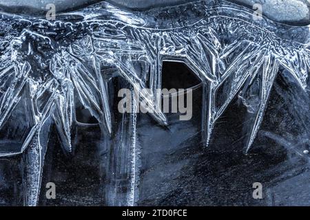 A close-up view of the captivating patterns formed by ice crystals on a dark frozen surface, highlighting nature's geometric artistry. Stock Photo