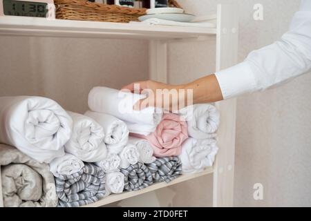 Crop hands of anonymous female massage therapist arranging clean rolled up white towels on shelf while working in luxurious spa salon Stock Photo