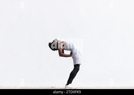 Side view full body of African American flexible sportsman in activewear standing and stretching back muscles while exercising against white backgroun Stock Photo