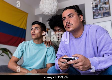 Multiracial curious male friends while sitting together with young man playing video game over console on sofa in living room Stock Photo