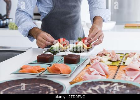 Crop anonymous male cook in apron putting strawberries on pineapple while preparing delicious breakfast in kitchen Stock Photo