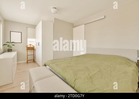 Green duvet on comfortable bed near drawer chest in white light bedroom at modern house Stock Photo