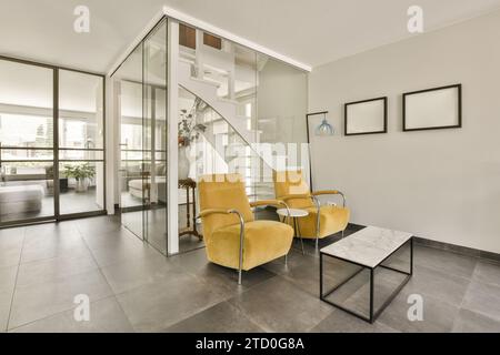 Yellow armchairs with marble coffee table against staircase behind glass wall in spacious room at modern house Stock Photo