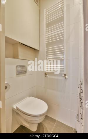 White toilet seat and radiator mounted in tiled walls in small restroom at modern apartment with cabinet Stock Photo