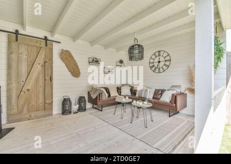 Long comfortable couch and coffee table in spacious patio of luxurious house with clock and decors on white wall Stock Photo