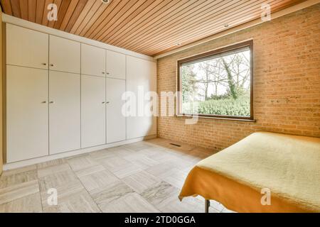 Comfortable bed with ornamental blanket placed near glass window and wardrobe in light bedroom Stock Photo
