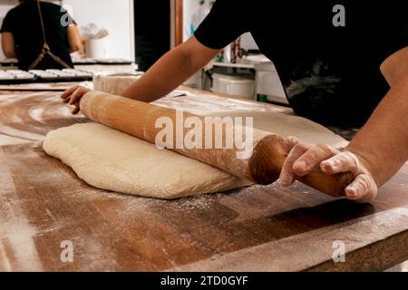 Crop hands of unrecognizable male chef rolling soft dough with wooden rolling pin on table in kitchen during cooking process at bakehouse Stock Photo