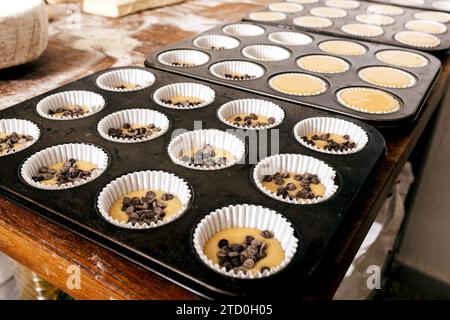 Closeup of metallic muffins tray with cupcake batter and chocolate chips in paper molds arranged on table for baking in bakehouse Stock Photo