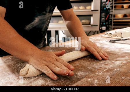 Crop hands of anonymous male cook in casuals kneading dough on wooden table with flour while preparing bread in kitchen of bakehouse Stock Photo