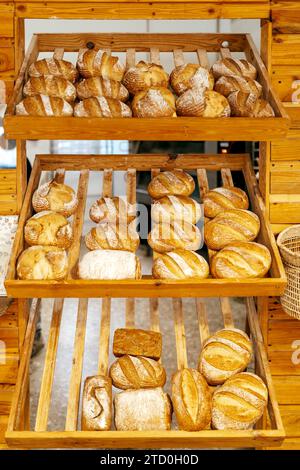 Various freshly baked tasty loaves of breads with crunchy crust placed on wooden shelves for display in bakery store Stock Photo