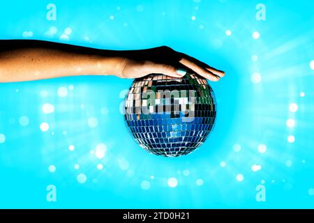 Cropped hand of anonymous woman holding disco ball against illuminated bright blue background with lens flare Stock Photo